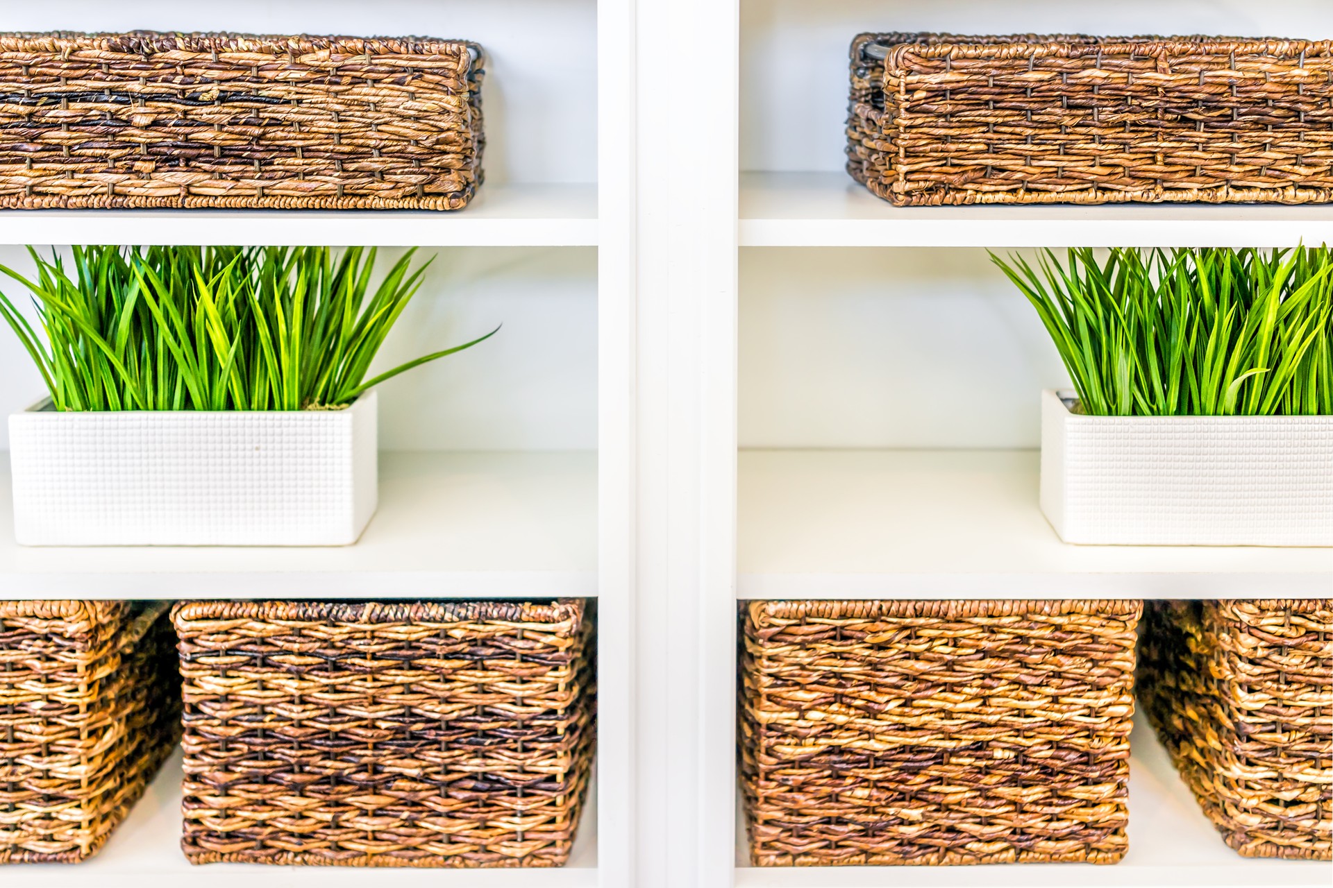 Closeup of white, modern, minimalist shelves in kitchen or living room with woven baskets and green plants pots, containers